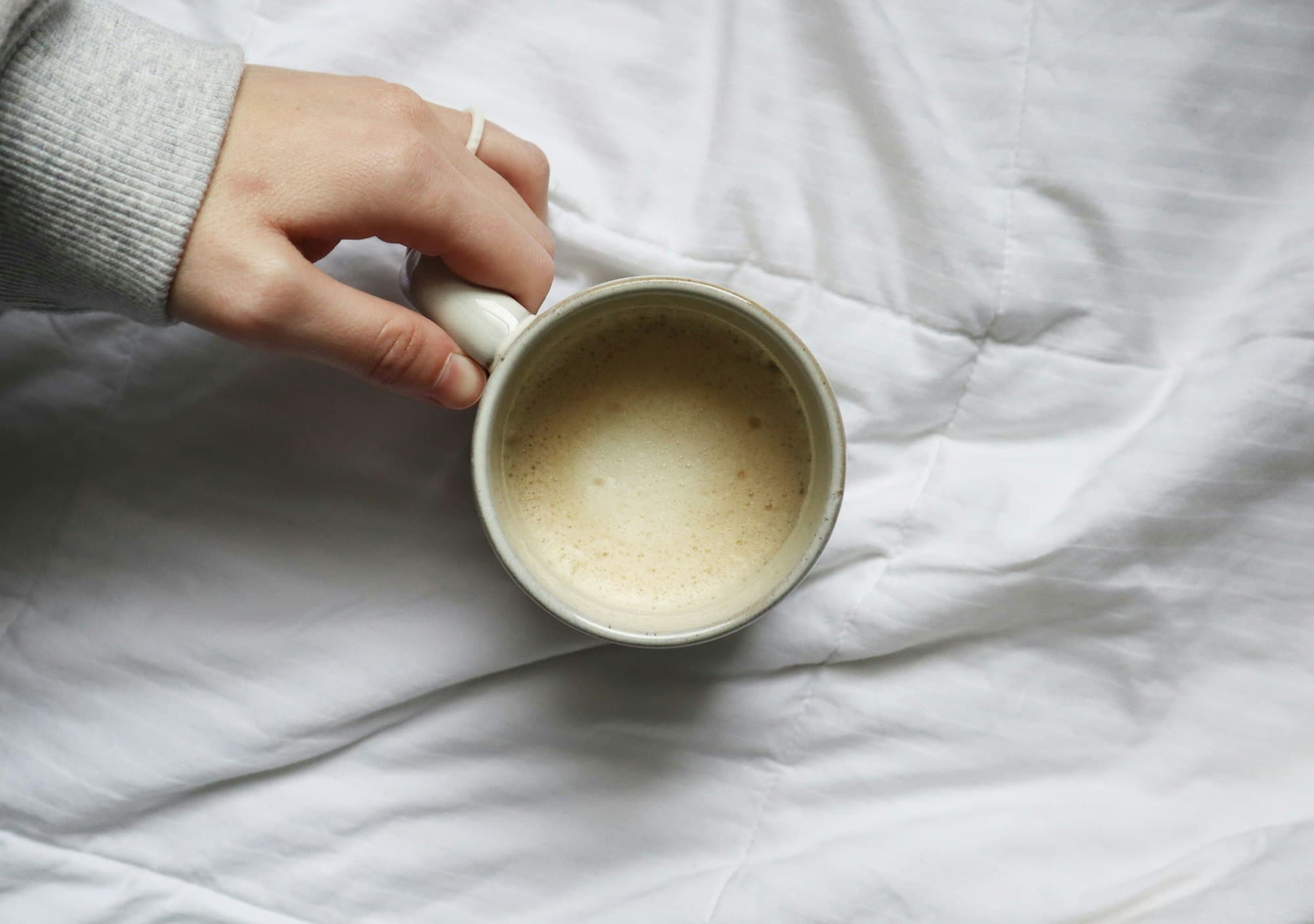 Mână ținând o ceașcă de cafea pe un pat alb